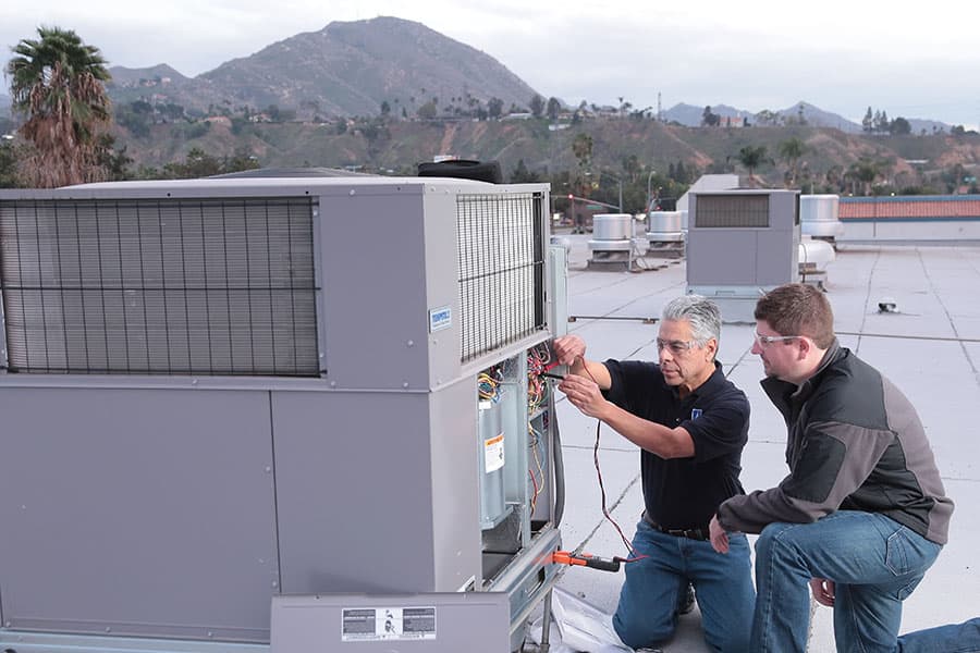 A Summit College student and professor working on a roof air conditioning unit
